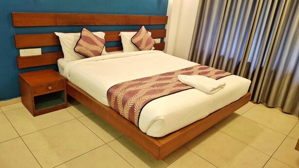 A hotel room with a wooden bed, a nightstand, and a curtain. - Hotel Wayanad gate (Vythiri)