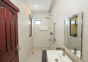 Un bagno con parete in marmo, porta in legno, lavandino bianco, uno specchio e una doccia.