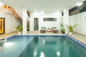 Una piscina interna con sedie a sdraio, piante in vaso e una scala.