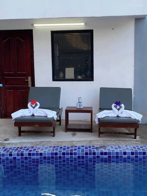 Two lounge chairs with towels shaped like swans, a small table with a water bottle, and a pool with blue tiles. - Sreng Angkor Hotel (Krong Siem Reap)