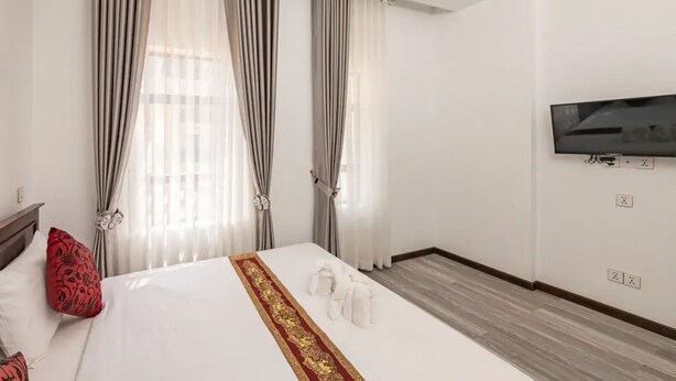 Une chambre d’hôtel avec un grand lit, un téléviseur fixé au mur et des rideaux aux fenêtres.