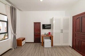 Una habitació amb escriptori de fusta, televisió, nevera petita i armari.