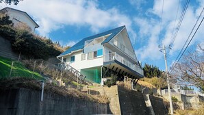 Ein zweistöckiges Haus mit blauem Dach, einem Balkon im oberen Geschoss und einer Betonretmlade im Vordergrund.