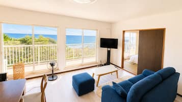 Un salon moderne avec un grand téléviseur, des canapés bleus, une table à manger et un balcon offrant une vue sur la mer.