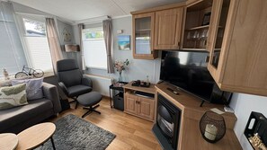 A modern living room with a sofa, armchair, TV, fireplace, and wooden cabinets. - Kamperland Beach Resort - 524 (Kamperland)