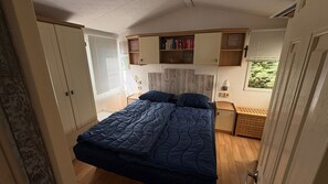 Ein Schlafzimmer mit einem Bett, Nachttischen, einem Kleiderschrank und einem Fenster mit Jalousien.