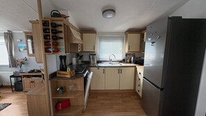 Eine kleine Küche mit Holzausstattung, einem schwarzen Kühlschrank und einem Fenster mit Jalousien.