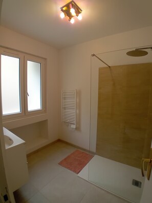 Une salle de bain avec une douche, une fenêtre, un porte-serviettes et un lavabo.