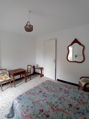 Une chambre à coucher comprenant un lit, un bureau, deux chaises, un miroir et un luminaire suspendu.