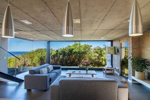 A modern living room with a large window, a sofa, a coffee table, and pendant lights. - Sea Through House (Knysna)