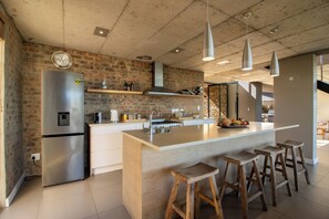 A modern kitchen with a stainless steel refrigerator, wooden stools, and a large island. - Sea Through House (Knysna)