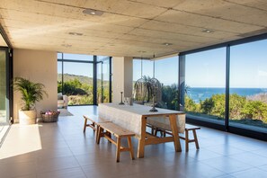 Une pièce spacieuse avec une grande table à manger, un banc et une vue sur la mer.