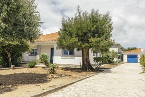 A residential building with a tiled roof, a blue door, and a garden with a large tree. - Cascais Boutique Retreat by Clama Retreats (Cascais)