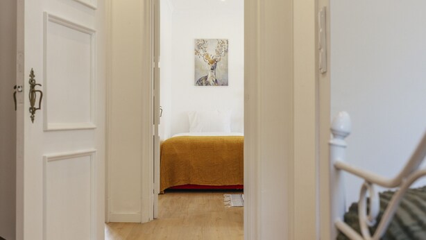 A hallway leading to a bedroom with a bed, a painting on the wall, and a staircase to the right. - Cascais Boutique Retreat by Clama Retreats (Cascais)