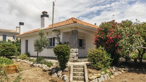 A two-story house with a tiled roof, a stone chimney, and a small garden with various plants and a flowering bush. - Cascais Boutique Retreat by Clama Retreats (Cascais)