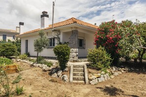 A two-story house with a tiled roof, a stone chimney, and a small garden with various plants and a flowering bush. - Cascais Boutique Retreat by Clama Retreats (Cascais)