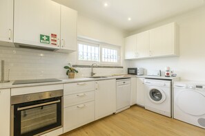 A modern kitchen with white cabinets, a built-in oven, a microwave, a sink, and a washing machine. - Cascais Boutique Retreat by Clama Retreats (Cascais)