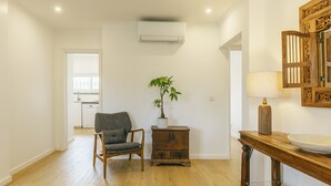 A room with a wooden floor, a chair, a small table with a lamp, a potted plant, and a wall-mounted air conditioning unit. - Cascais Boutique Retreat by Clama Retreats (Cascais)