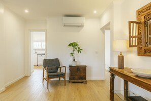 A room with a wooden floor, a chair, a small table with a lamp, a potted plant, and a wall-mounted air conditioning unit. - Cascais Boutique Retreat by Clama Retreats (Cascais)