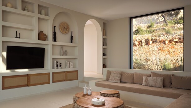 Een moderne woonkamer met een grote televisie, inbouwplanken, een ronde salontafel en uitzicht op een rotsachtig landschap.