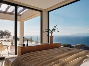 A bedroom with a large window, a bed, a bedside table, and a potted plant. - Luxury 6-bedroom villa in north Zakynthos | Private pool & sea views (Korithi)