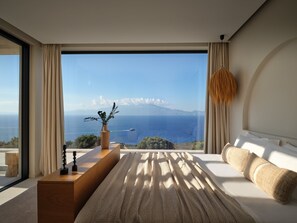 A bedroom with a large window, a bed, a bedside table, and a view of the sea and mountains. - Luxury 6-bedroom villa in north Zakynthos | Private pool & sea views (Korithi)