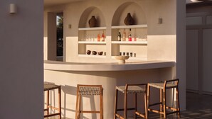 Een bar met een toonbank, planken met flessen, glazen en een schaal. Drie houten stoelen met geweven zittingen.