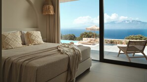 Een slaapkamer met een groot bed, uitzicht op zee en een balkon met een stoel.