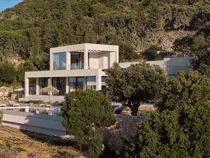 Un bâtiment moderne à deux étages, doté d’une piscine, entouré d’arbres et de collines.