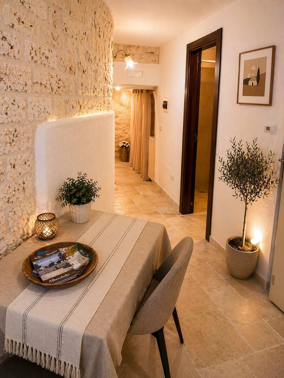 Una camera d'albergo accogliente con un muro in pietra, un'area pranzo con tavolo e sedie, una pianta in vaso e una porta che conduce a un'altra stanza.