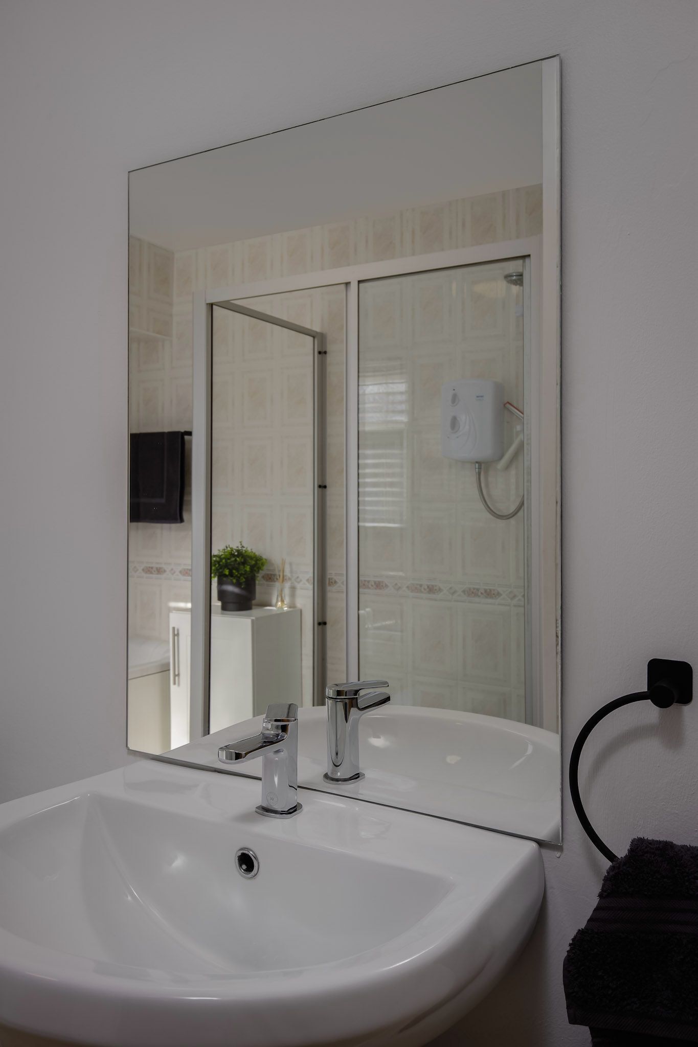 Een badkamer met een witte wasbak, een spiegel en een handdoekhouder.