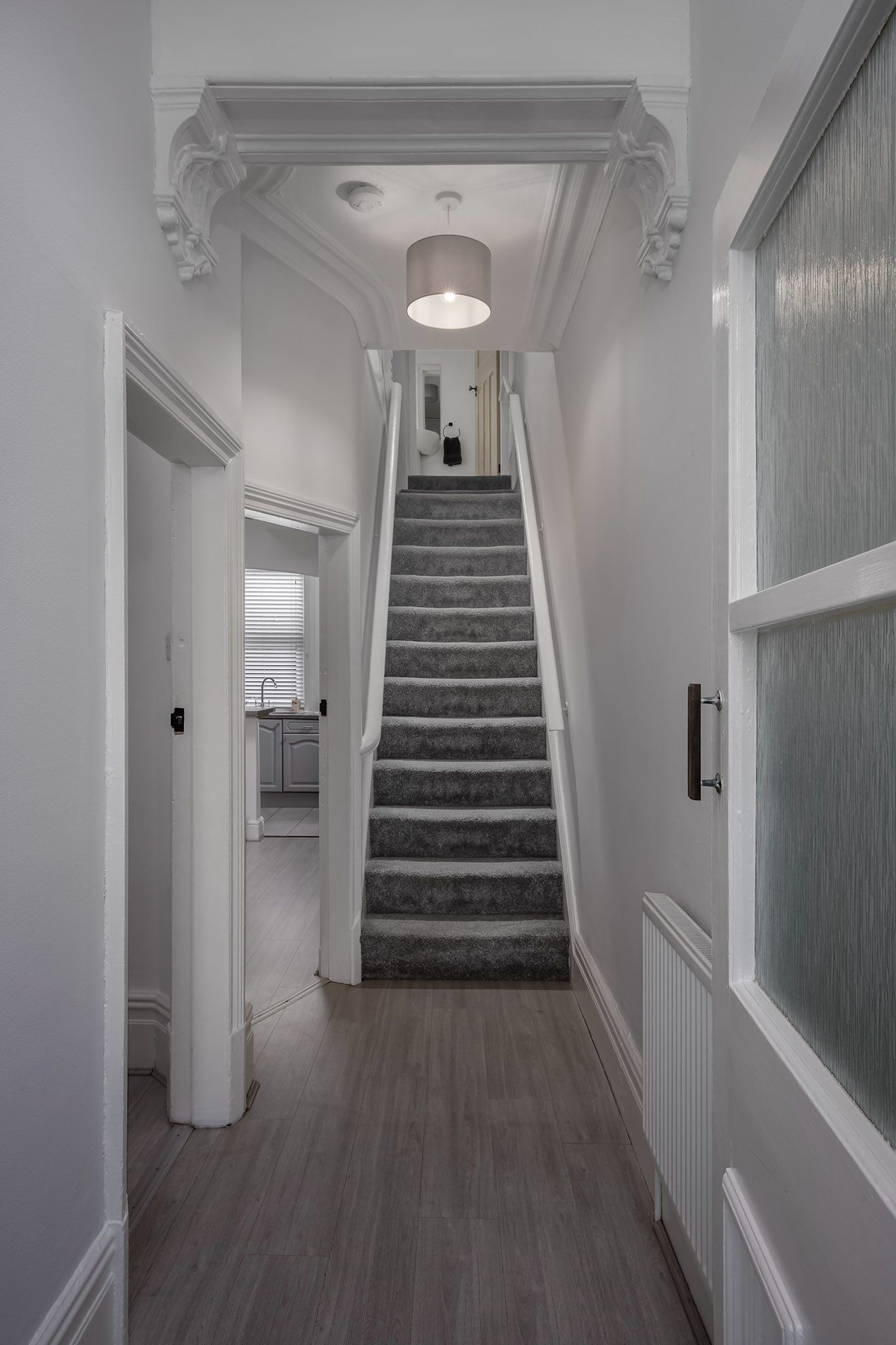 A staircase with a grey carpet, white walls, and a ceiling light fixture.