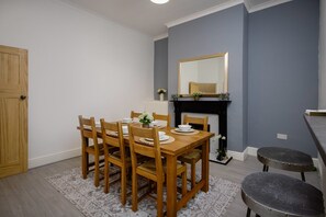 Een eetgedeelte met een houten tafel en stoelen, een open haard en een spiegel erboven.