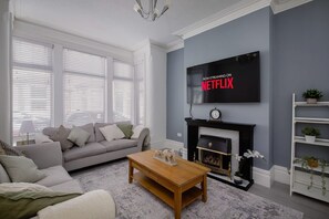 Ein Wohnzimmer mit Kamin, einer Couch, einem Couchtisch und einem an der Wand befestigten Fernseher.