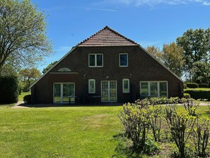 Een tweelaags bakstenen huis met een puntige kap, grote ramen en een gazon ervoor.
