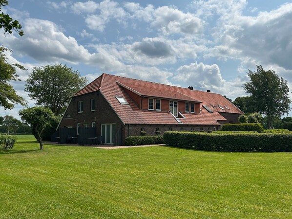 Een groot, twee verdiepingen tellend, bakstenen huis met een schuin dak, een kleine garage en een verzorgd gazon.