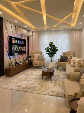 Un salon moderne avec un téléviseur à écran plat fixé au mur, une grande plante en pot et un ensemble de canapés de couleur beige.