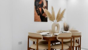 Zona pranzo con tavolo rotondo, sei sedie, un vaso con pampa e un quadro appeso al muro.
