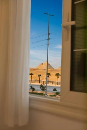 A view through a window of a desert landscape with pyramids and palm trees. - pyramids view luxury apartment (Pyramids Gardens)