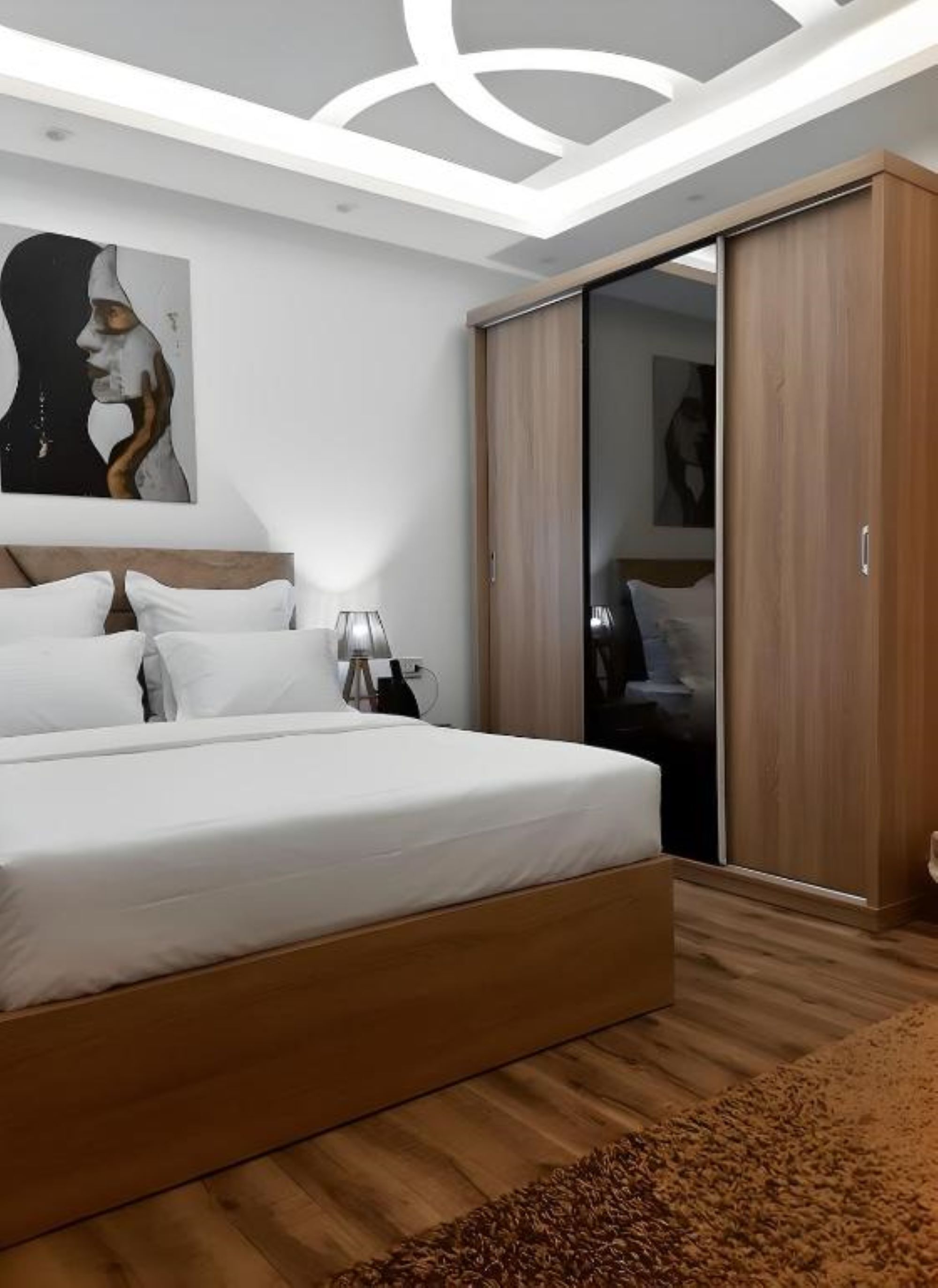 Une chambre moderne avec un grand lit, un plancher en bois et un plafond orné de luminaires aux motifs géométriques.