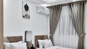 Una camera d'albergo con due letti, una lampada a soffitto, un condizionatore d'aria e una finestra con tende.