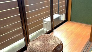 Une pièce dotée d'un plancher en bois, d'une chaise en osier et d'une porte-fenêtre coulissante donnant sur un espace extérieur délimité par une clôture en bois.