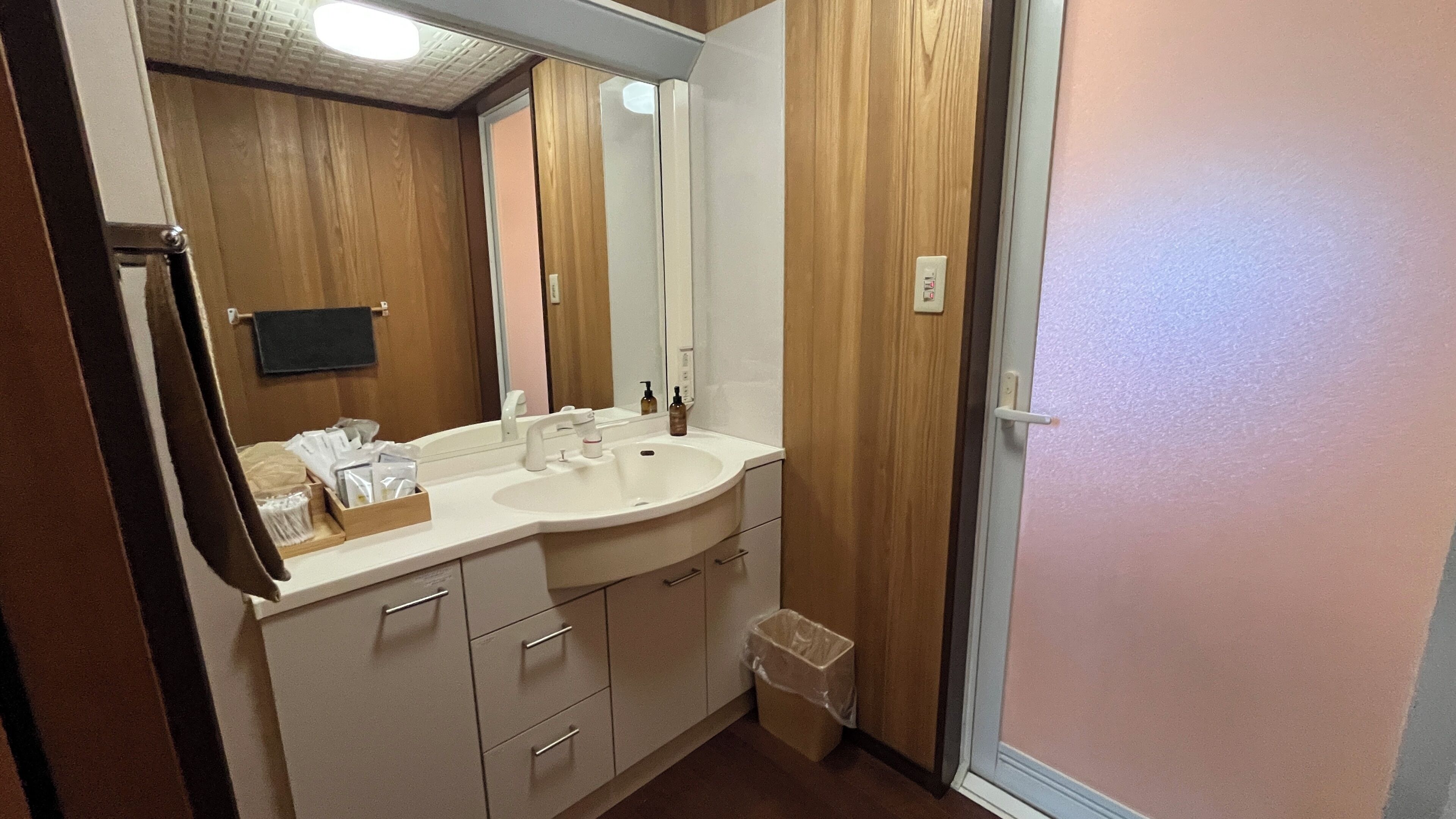 Un baño con lavamanos doble, paneles de madera, un espejo y un cubo de basura.