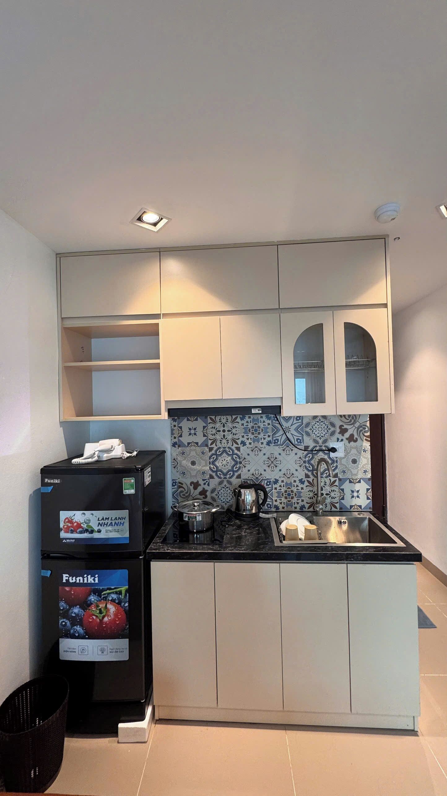 Una cocina compacta con armarios blancos, un refrigerador negro y un salpicadero de azulejos.