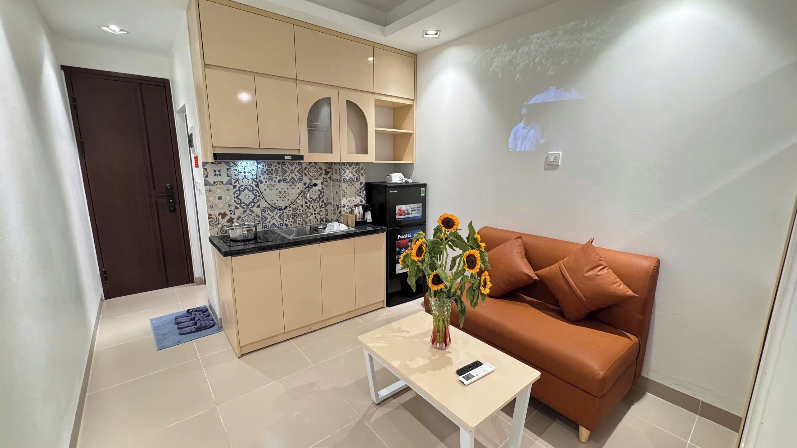 Un espacio habitable pequeño con kitchenette, un sofá, una mesa de centro y un florero con flores.