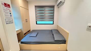 A small, single-bed room with a window, a wardrobe, and a wall-mounted air conditioner.