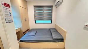 Una habitación pequeña con cama individual, ventana, armario y aire acondicionado instalado en la pared.