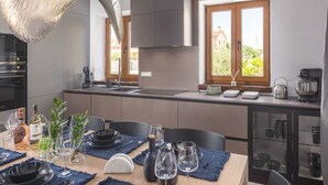 A modern kitchen with a dining area set for a meal, featuring a large window, built-in appliances, and a clean, organized layout. - Vila Aurelia by Villas Guide (Cabrunici)