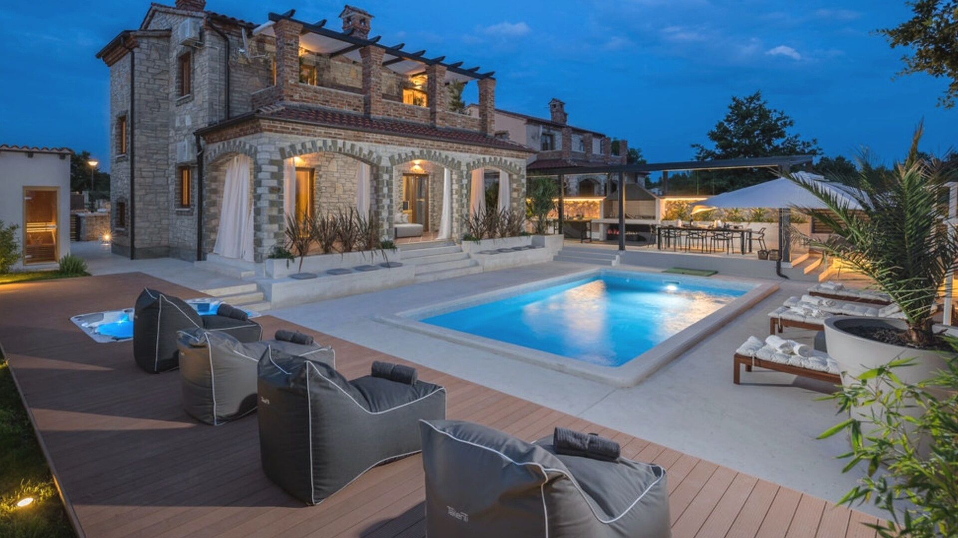 A poolside area with a stone building, outdoor seating, and a hot tub.