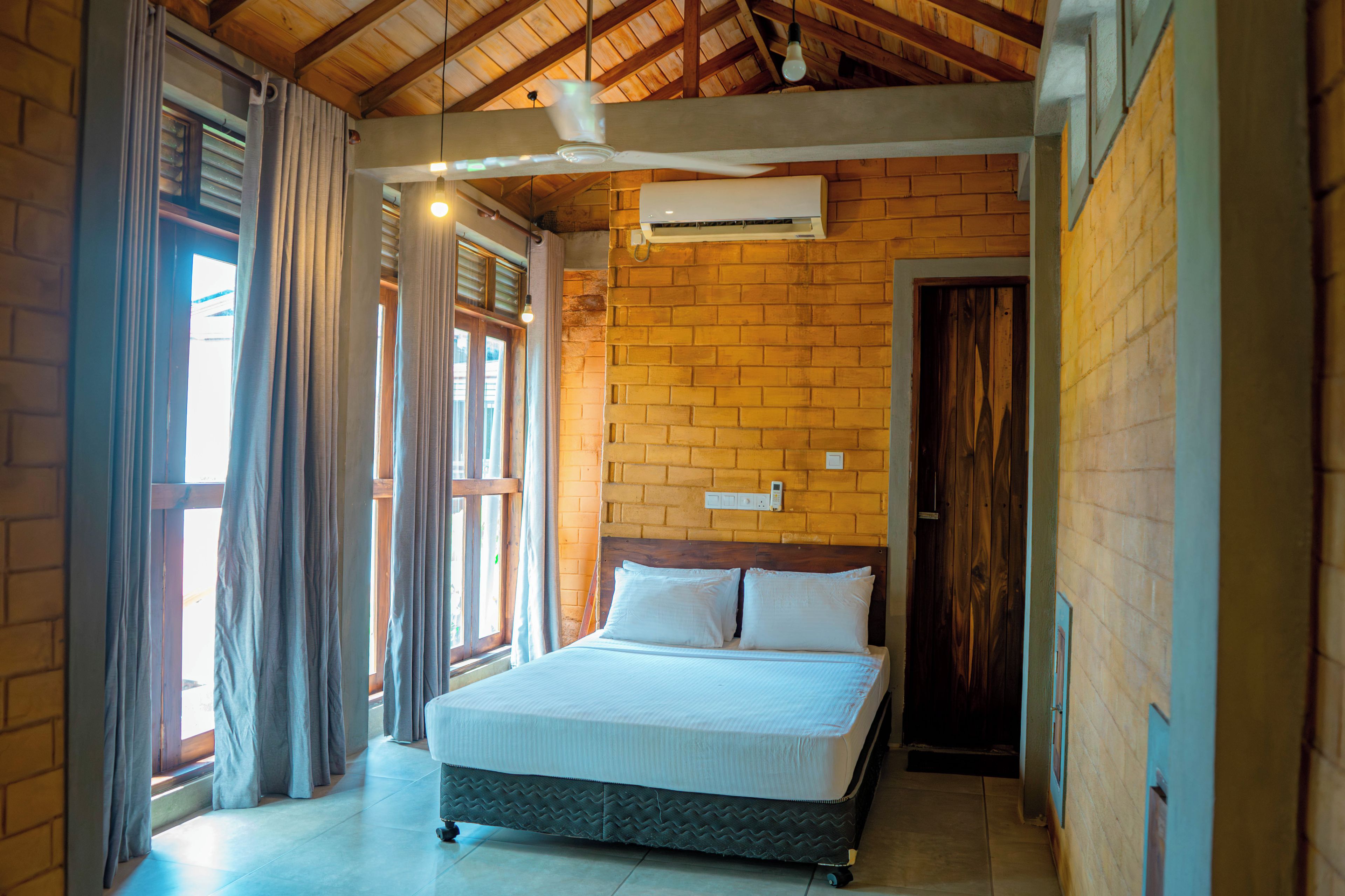 Un dormitorio con cama, ventana con cortinas, pared de ladrillo y aire acondicionado.